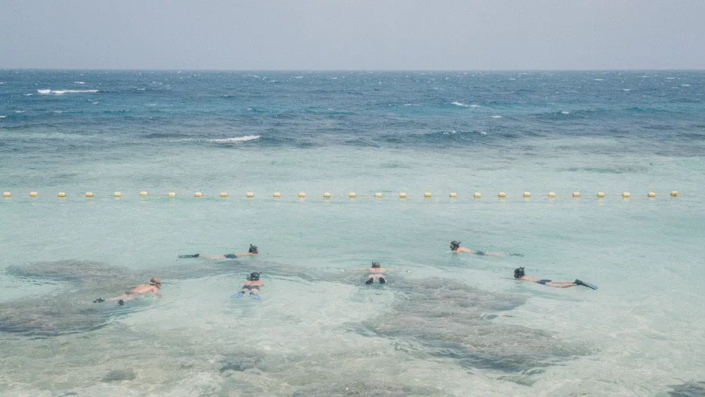 Alignement de bouées jaunes dans un lagon, séparant une zone calme proche du rivage de l’océan plus agité au large.