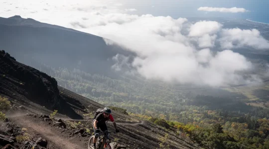 Vttiste en descente sur un sentier volcanique au Maido, avec la mer au loin et un grand espace de ciel libre pour le texte.