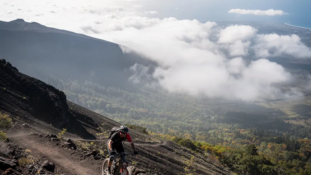 Vttiste en descente sur un sentier volcanique au Maido, avec la mer au loin et un grand espace de ciel libre pour le texte.